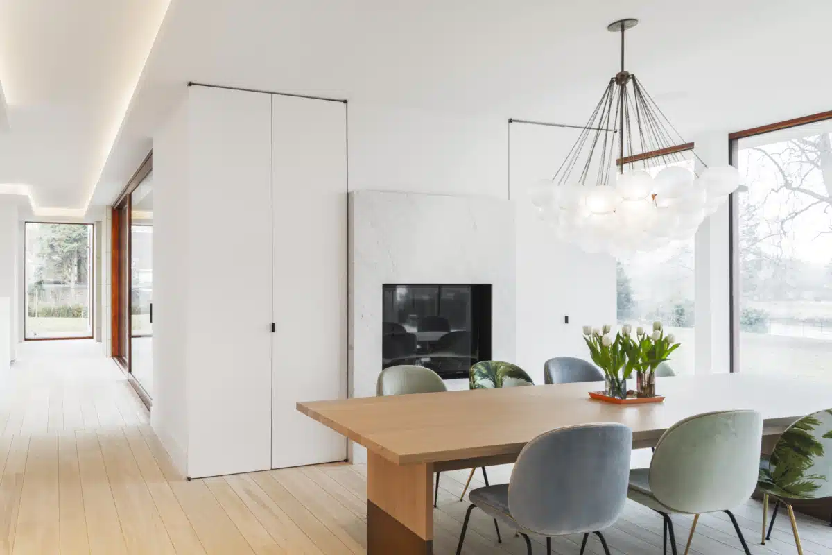 Eetkamer met houten tafel en elegante stoelen, omringd door veel natuurlijk licht.