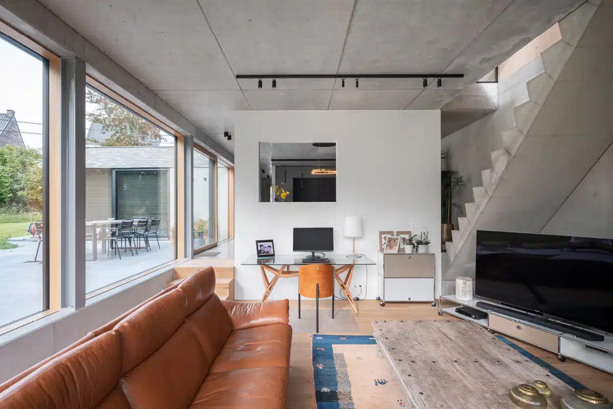 Industriële woonkamer met grote ramen en betonnen plafond, afgewerkt door In't Wit.