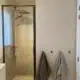 Totale badkamerrenovatie in De Haan door In't Kleur en In't Wit. Op de foto zien we een douche met zwarte omranding, mortex op de muren, kapstokjes voor de handdoeken waar twee handdoeken aanhangen.