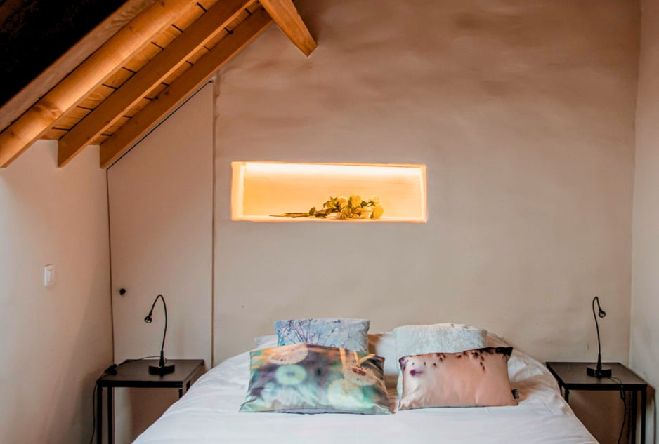 Moderne slaapkamer met golvend pleisterwerk, houten balken en ingebouwde verlichte nis in landelijke woning
