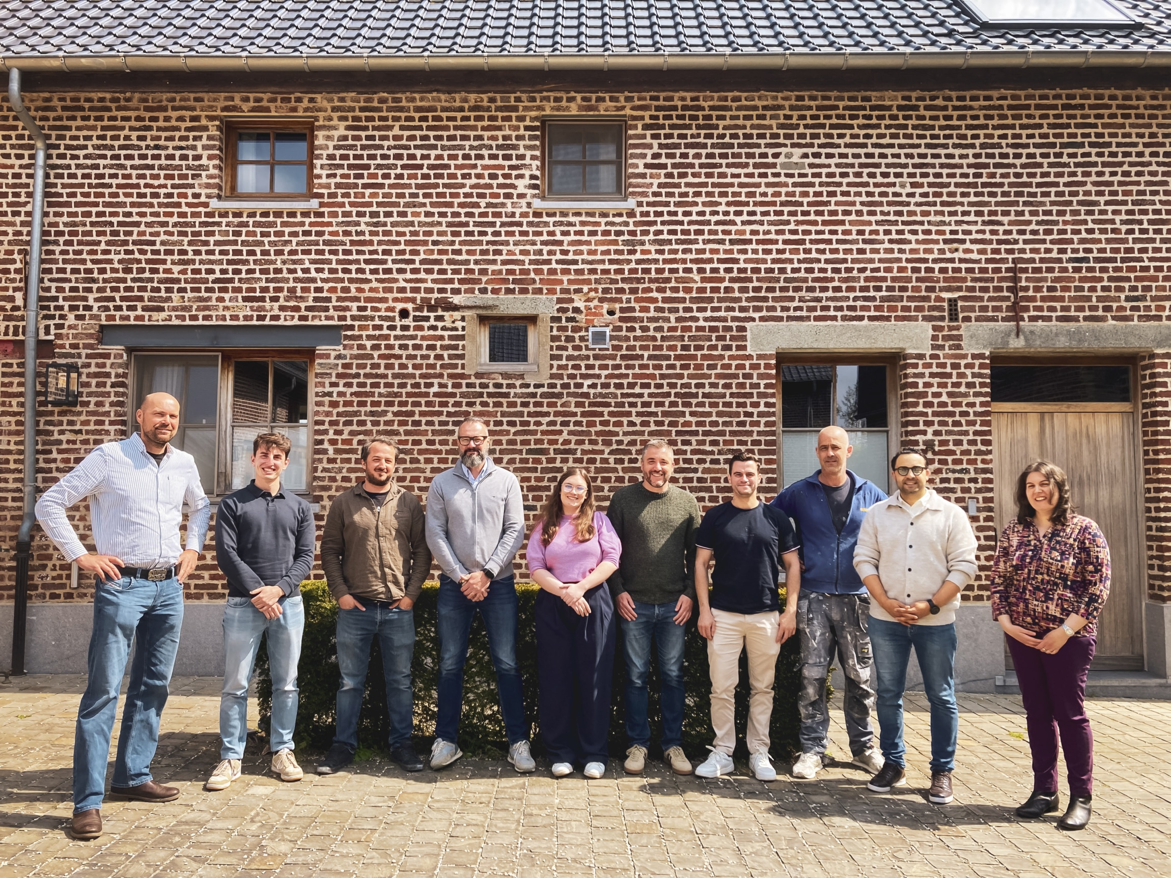 In't Wit pleisterwerkbedrijf team poseert voor bakstenen gebouw - professionele vakmensen in de bouw