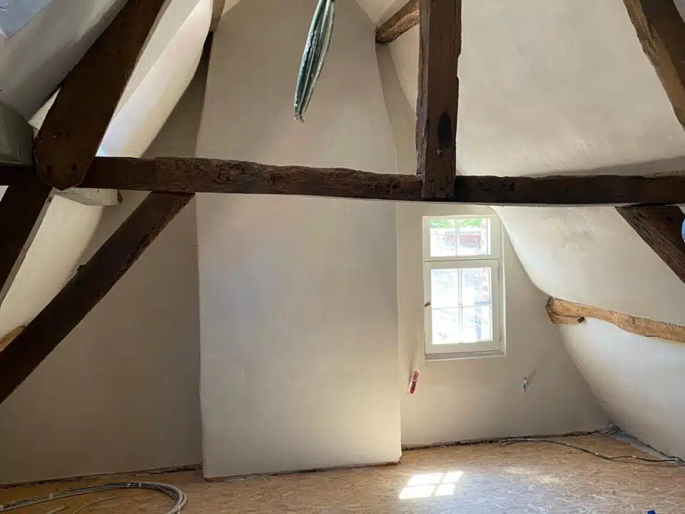 Gerenoveerde zolder met gepleisterde witte muren, houten dakbalken, OSB-vloer en elektrische bedrading tijdens renovatieproje